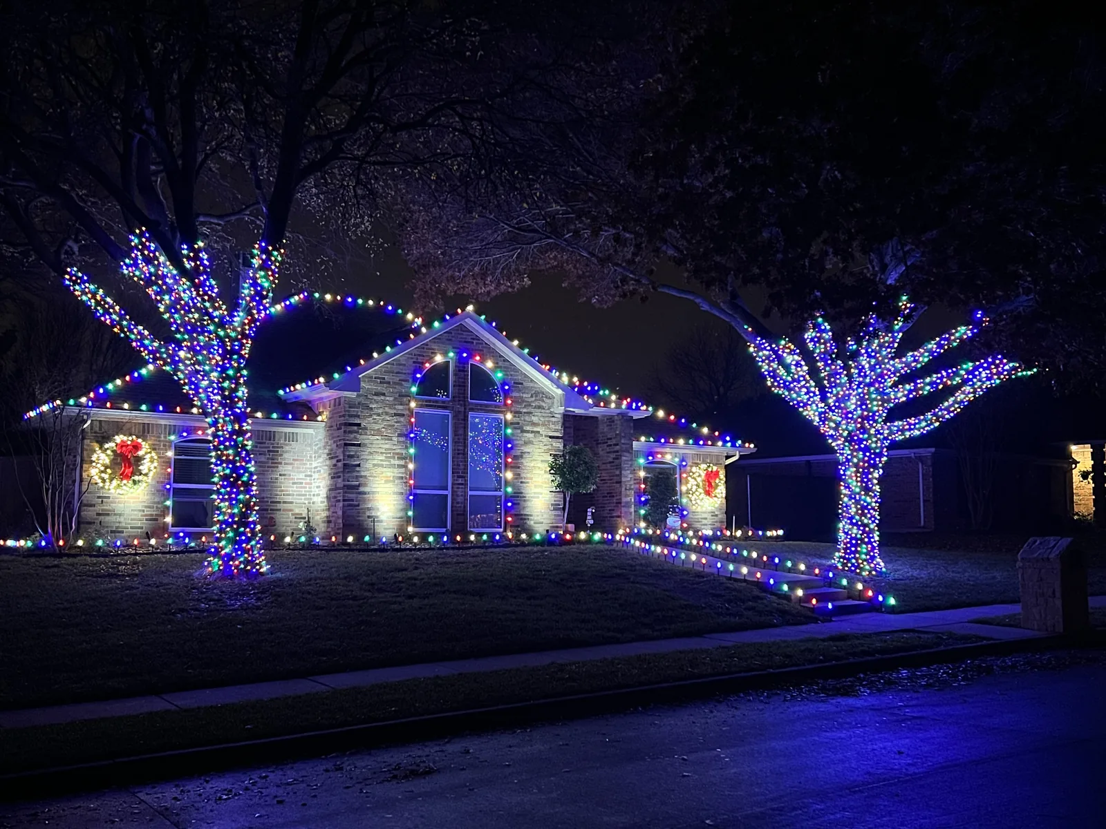 Christmas light installation Allen TX — festive multicolor roofline and wrapped trees on a family home