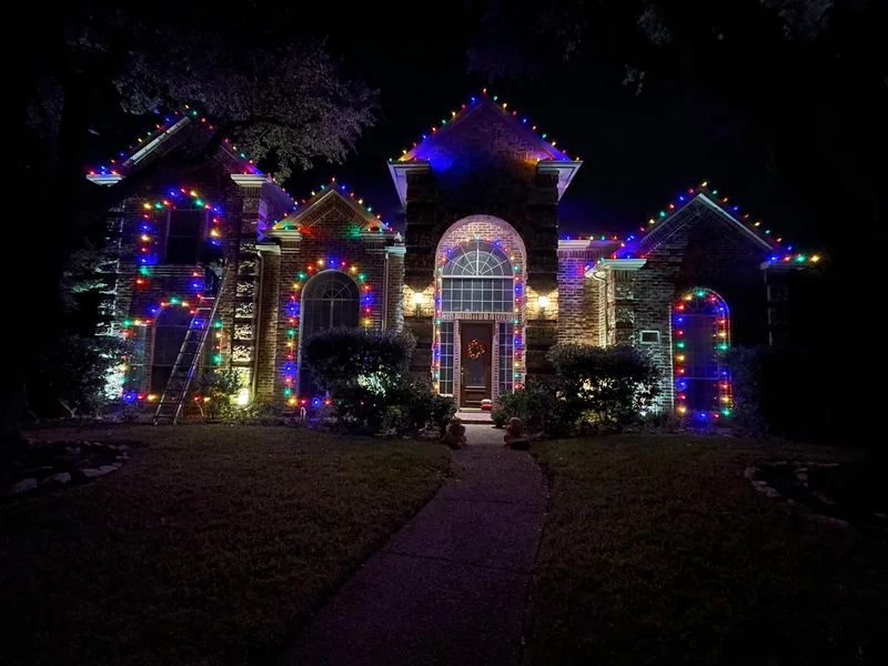 Christmas light installation by Christmas Lights Experts DFW &mdash; multicolor C9 LED roofline and arched windows on a stone home during installation