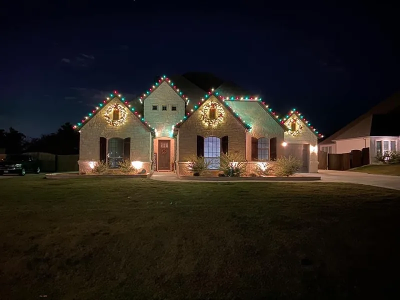 Christmas light installation by Christmas Lights Experts DFW &mdash; single-story stone home with a warm white C9 roofline, multicolor accents and lit wreaths