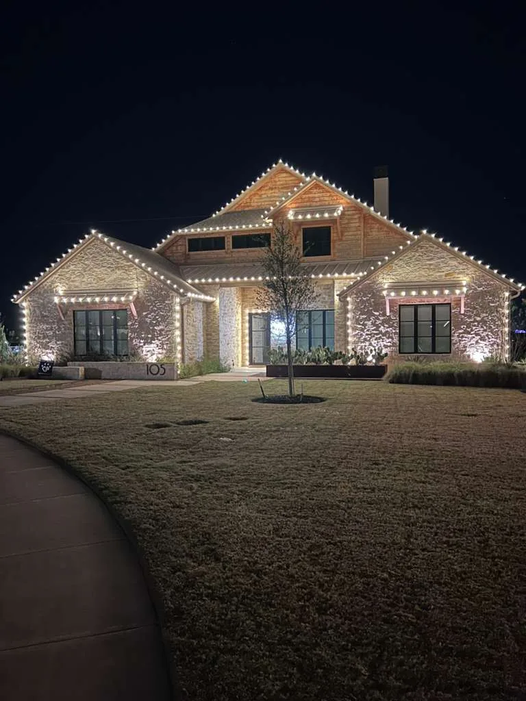 Christmas light installation Frisco TX — warm white roofline and wreaths on a stone home