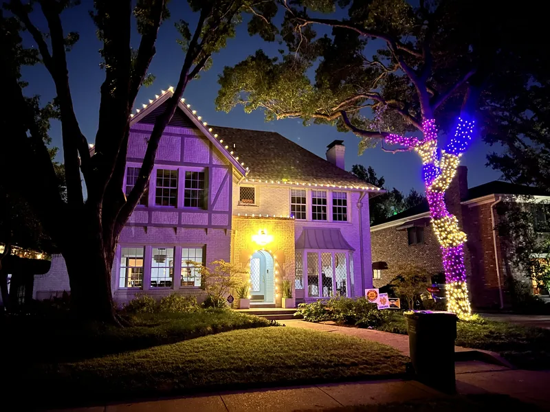 Christmas light installation by Christmas Lights Experts DFW &mdash; Tudor-style home with a warm white roofline and a tree wrapped in multicolor lights