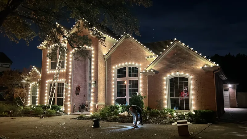 Christmas light installation by Christmas Lights Experts DFW &mdash; warm white C9 LED roofline on a two-story brick home, crew finishing the install at dusk
