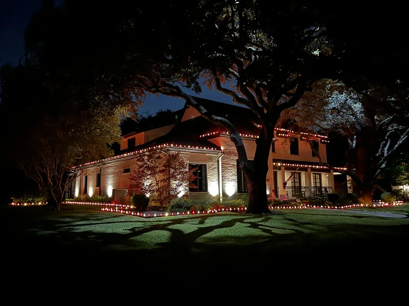 Christmas light installation by Christmas Lights Experts DFW &mdash; single-story brick home with a warm white roofline and lit landscape beds