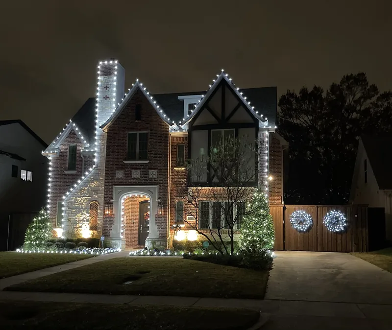 Christmas light installation by Christmas Lights Experts DFW &mdash; Tudor-style two-story home with a warm white roofline and lit wreaths on the garage